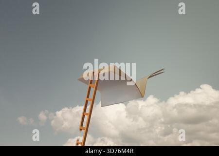A book page opens like a bird with a ladder reaching for it under a cloudy sky. Stock Photo