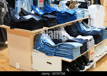 Stacks of folded blue, black, and gray denim jeans displayed on wooden shelving in a retail clothing store with a -30% sign. High quality photo Stock Photo