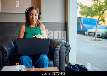 Woman working remotely with laptop and headphones in cafe Stock Photo