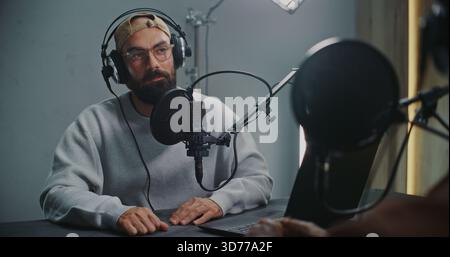 Podcast Host With Open Laptop Listening to Guest, Both Using Headphones and High End Microphones. Concept Authentic Dialogue, Creative Exchange in Modern Media Space, and Relaxed Storytelling Vibe. Stock Photo