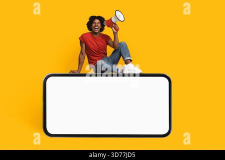 Man With Megaphone Sits on Blank Screen Against Bright Yellow Background Stock Photo
