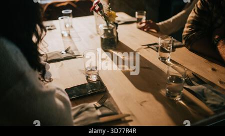 A woman sits at a table with a man and a child. The table is set with glasses, forks, knives, and spoons. The woman is looking at her phone while the Stock Photo
