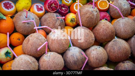 A vibrant assortment of fresh tropical fruits is displayed, featuring whole coconuts with straws, oranges, and colorful pomegranates at a local market Stock Photo