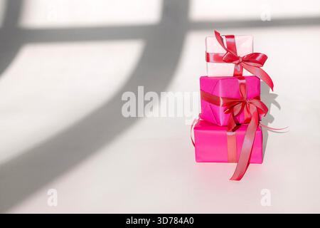 Three gifts in bright packaging and satin bows on a white background. Present boxes in different colors with pink ribbons. Copy space Stock Photo