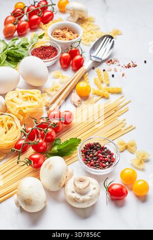Food background with different kinds of pasta, tomatoes, herbs, mushrooms, eggs, seasonings scattered on light marble background, top view. Italian cuisine concept Stock Photo