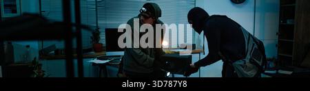 Header of Young Adult Men Wearing Masks Removing Safe from Office during Nighttime Heist Stock Photo