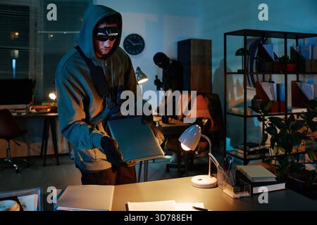 Young Caucasian Man Stealing Documents in Office at Night with Accomplice Stock Photo