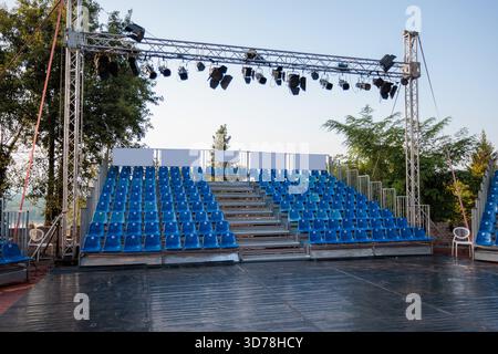 Empty outdoor stage with rows of blue seats under a clear sky in the evening Stock Photo
