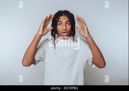A young man with curly hair stands in a studio, expressing surprise. Stock Photo
