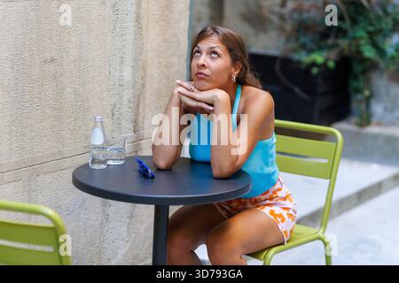young woman sits at a table, lost in thought and being bored Stock Photo