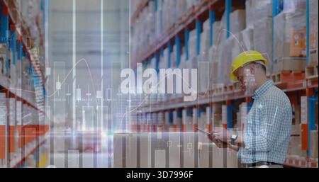 Warehouse worker wearing yellow hat operating tablet on boxes in aisle, racks, charts, copy space Stock Photo