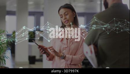 Pointing woman in pink blouse holding tablet and speaking in office, graph overlay, papers Stock Photo