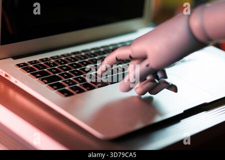 Robot hand interacting with laptop keyboard Stock Photo