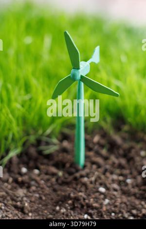 Small green wind turbine model placed in soil with green grass background Stock Photo