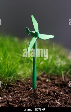 Small green wind turbine model placed in soil with green grass background Stock Photo