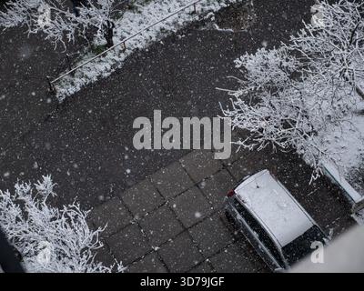 Large fluffy snowflakes falling over a square tiled building entrance and a grey car parked at the porch. Beautiful white trees covered in snow. Stock Photo
