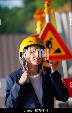 Young woman putting on a yellow helmet in front of a construction site Stock Photo