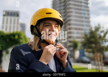 Young woman with teeth braces putting on a yellow helmet while preparing for cycling in the city Stock Photo