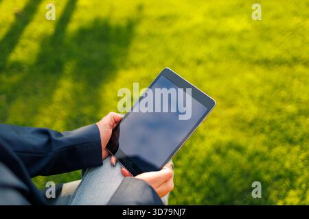 closeup of woman holding a tablet while sitting on green grass Stock Photo