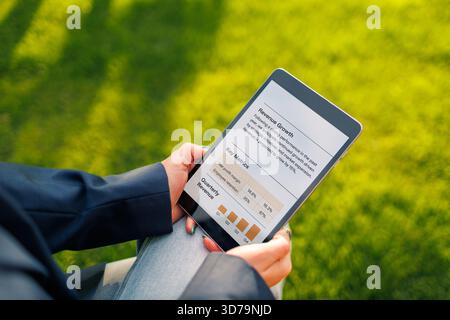 Person using tablet to analyze market data in a sunny outdoor park setting Stock Photo