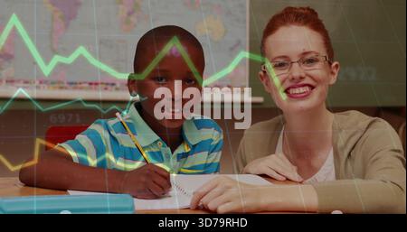 Guiding teacher in cardigan leaning beside kid writing in class using pencil notebook graph overlay Stock Photo