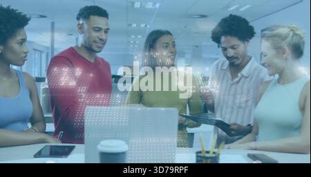 Collaborating team in business casual leaning over laptop in open-plan office, holding tablet Stock Photo