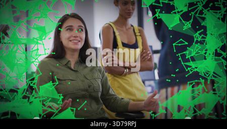 Presenting seated woman in olive shirt at office, colleague in yellow overalls watching, AR overlay Stock Photo