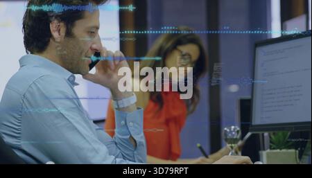Talking blue-shirt man on phone, viewing code monitor at desk, red-clad woman noting waveform Stock Photo