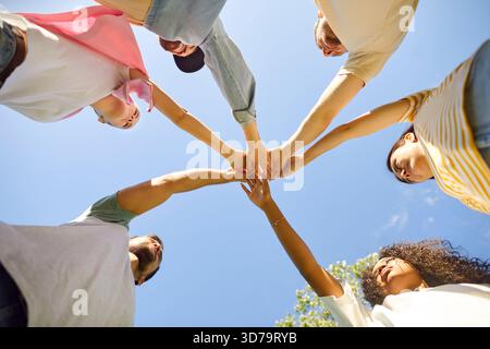 Group of diverse friends standing in circle under blue summer sky and stacking hands Stock Photo