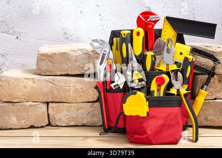 Belt bag with various hand tools leaning on an old bricks on a wooden table with copy space for text. Selective focus. Stock Photo