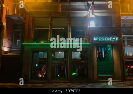 McCooley's Irish bar in Liverpool's Cavern Quarter at night. The entrance is illuminated by bright, cool-green neon lighting. Stock Photo