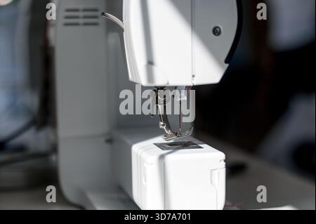 Close-up of the presser foot and needle of a modern white sewing machine. Part of a white household sewing machine with a metal working element. Stock Photo