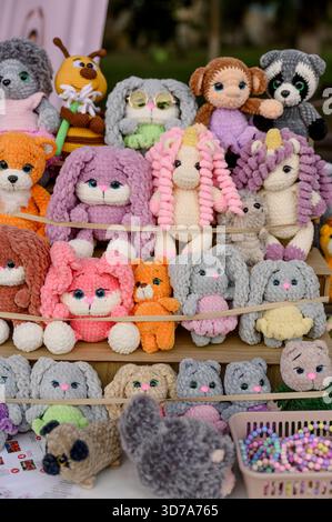 A stand with a variety of brightly colored knitted toys at a handicraft fair. Plush rabbits, unicorns, cats, hand-knitted bears on the shelves. Stock Photo
