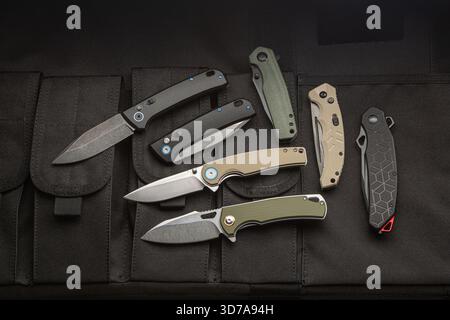 A collection of six modern folding knives displayed on a black tactical gear surface. Stock Photo
