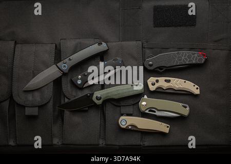 A collection of six modern folding knives displayed on a black tactical gear surface. Stock Photo