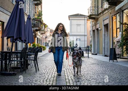 Young woman walking with her spotted dog on a charming cobblestone in european city street Stock Photo