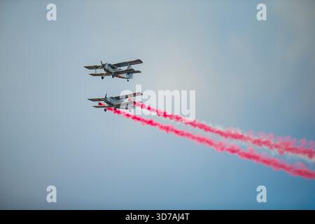 Two light propeller aircraft flying in tight formation with long red smoke trails extending behind their wings against soft sky gradient Stock Photo