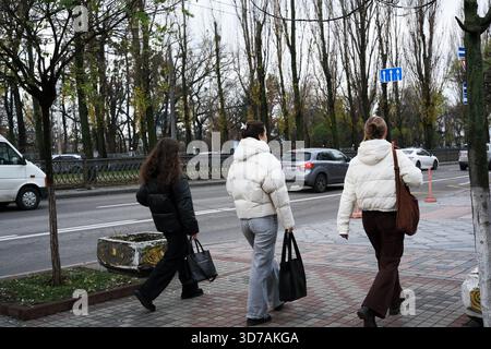 Three women stroll down a city street lined with trees in fall colors. November 24, 2025, Kyiv, Ukraine, Shevchenko Boulevard Stock Photo