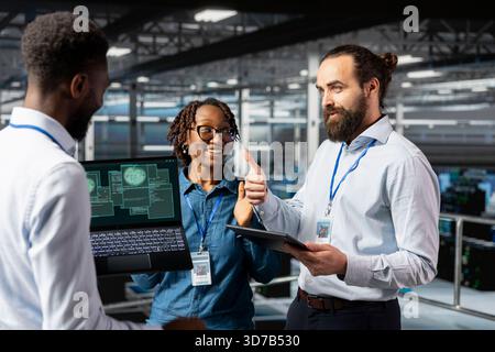 System administrator congratulating his team with a thumbs up, feeling pleased with his employees and enjoying server hub achievement together. Happy satisfied engineers in data center. Stock Photo
