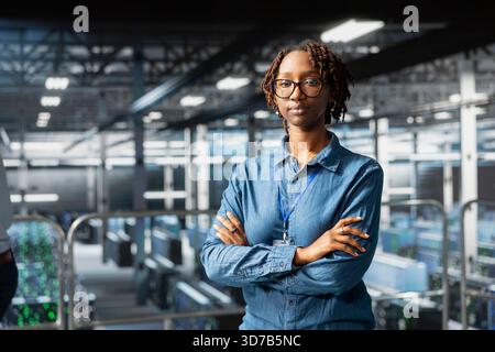 Portrait of smiling african american engineer running diagnostics on AI tools, using deep learning equipment to identify errors. Happy woman working to prevent failure and minimize downtime. Stock Photo