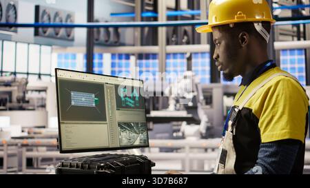 Smart factory employee typing on PC keyboard, testing automated systems, doing maintenance. Industry 4.0 plant staff member using computer to inspect equipment and repair bugs, camera A Stock Photo