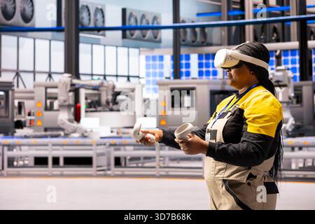 Female engineer wearing VR headset examines data insights to improve operational efficiency in smart factory. Technician using virtual reality in Industry 4.0 facility equipped with advanced sensors. Stock Photo