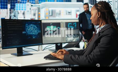 Software developer in photovoltaics factory using artificial intelligence to oversee robot arms placing solar panels on assembly lines. System administrator upgrading solar plant using AI, camera A Stock Photo