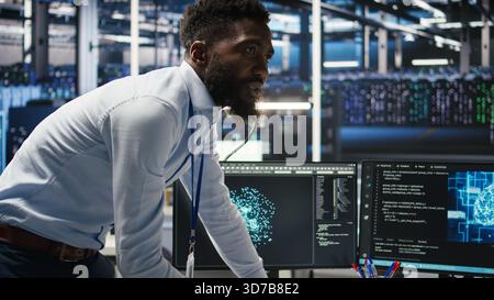 Server farm supervisor and man with disability adjust system settings based on AI analytics. Data center manager talking with technician in wheelchair overseeing automated node tree tool, camera A Stock Photo