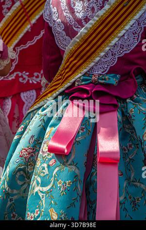 Close-up of a colourful traditional Fallas festival costume from Valencia with embroidered fabrics, pink satin ribbons, lace details, and a striped re Stock Photo