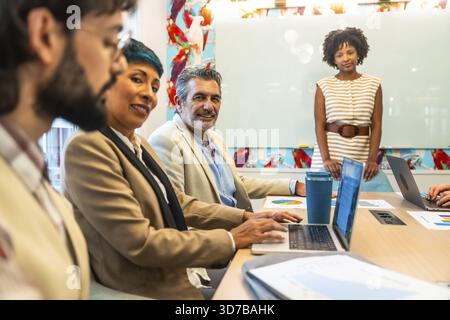 Diverse business colleagues holding a meeting or presentation, working and smiling in a colorful modern office space, discussing ideas and planning wo Stock Photo