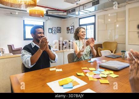 Diverse colleagues participating in a successful meeting, collaborating and brainstorming ideas using sticky notes, and applauding achievements in a m Stock Photo