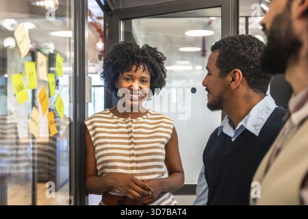 Smiling african american woman presenting ideas while discussing project strategies with diverse team members during a corporate brainstorming session Stock Photo