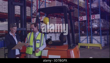 Checking woman in blazer and man in vest counting pallets in warehouse with orange forklift, helmet Stock Photo
