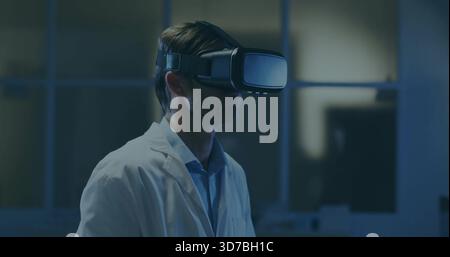 Standing scientist wearing virtual reality headset and lab coat in dim research room, with monitors Stock Photo